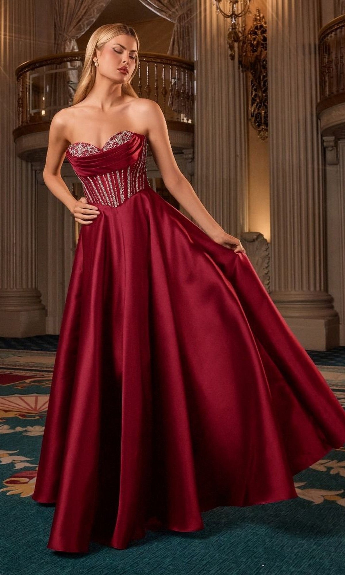 A woman wearing the Strapless Navy Blue Prom Gown, Ladivine CK2405, featuring a fitted bodice and floor-length silhouette, stands in an ornate room adorned with columns and chandeliers.